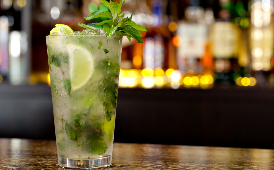 A tall glass filled with ice, lime and mint leaves, and a mint sprig