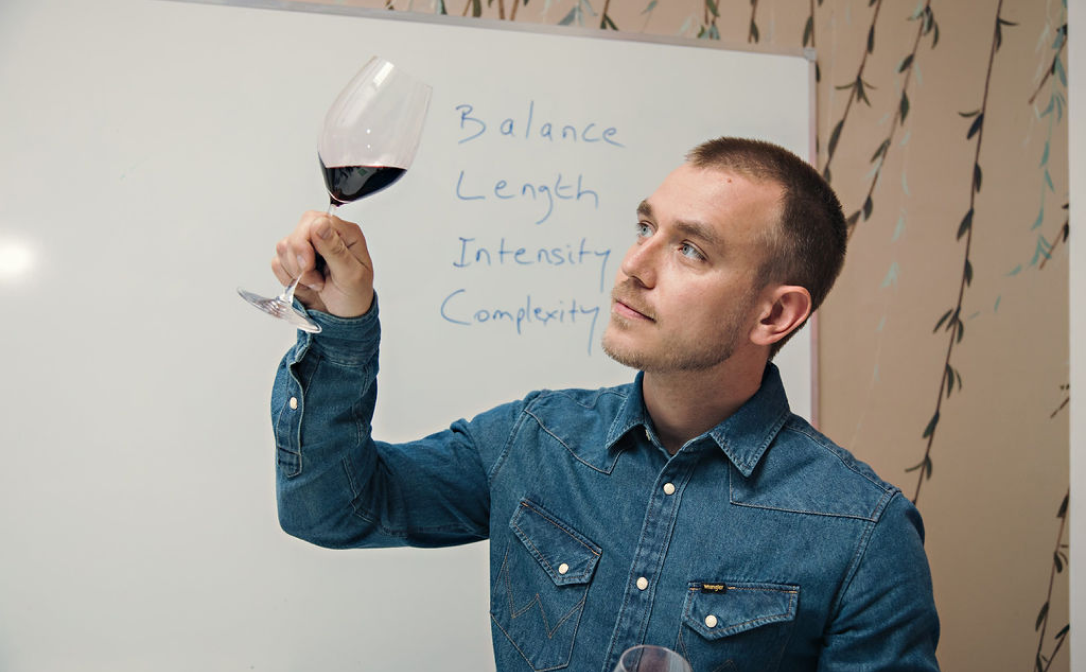 A man holding a glass of red wine up to the light