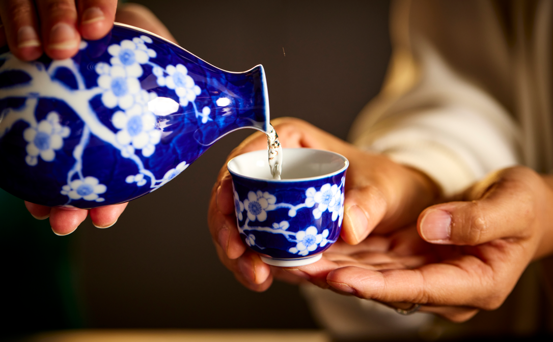 Sake being poured into a small blue and white ceramic cup