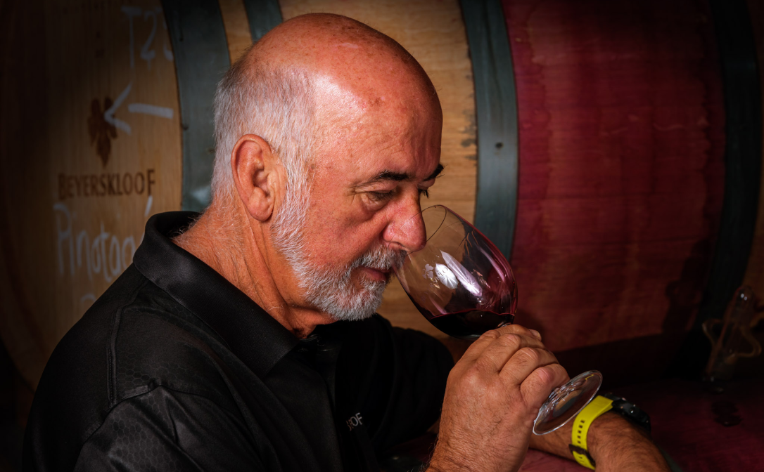 A man standing in front of wine barrels, smelling red wine in a large glass