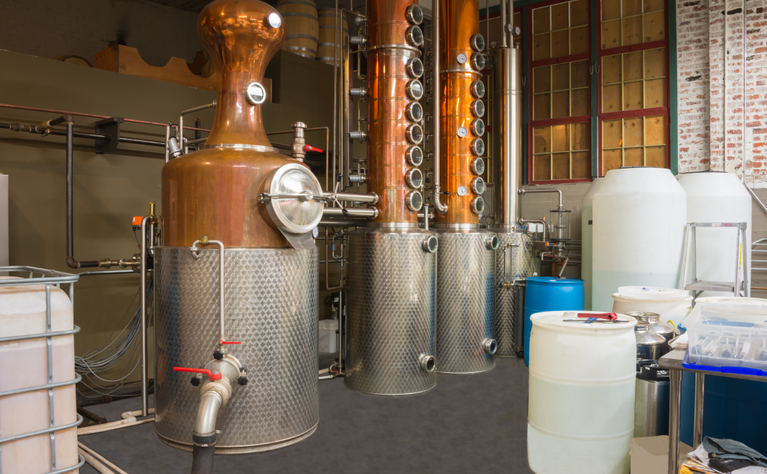 A column still made from copper in a distillery, surrounded by plastic barrels